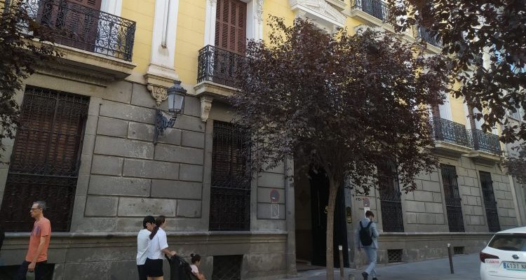 Fachada de la embajada de Chile en Madrid con árboles y personas caminando.