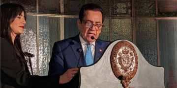 El embajador hablando en un evento con Crismeidy Ureña a su lado