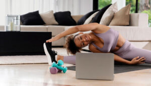 Mujer haciendo ejercicio en casa con mancuernas y computadora portátil