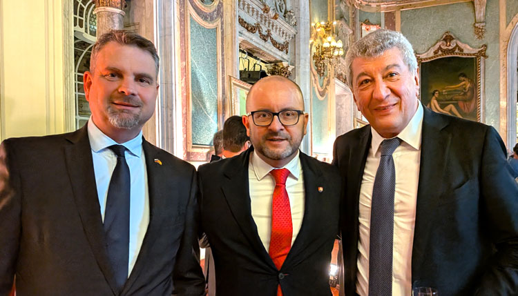 Tres hombres en traje en un evento diplomático en un salón elegante.