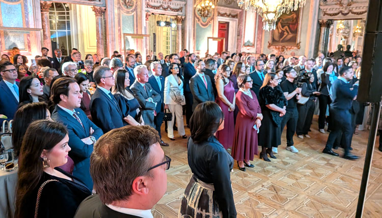 Multitud de asistentes en una recepción diplomática en un elegante salón.