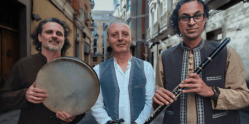 Cardamom Trío posando en una calle, con instrumentos musicales