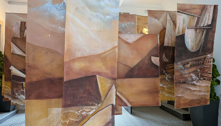 Instalación artística en la Embajada de Colombia con pinturas de barcos y paisajes.