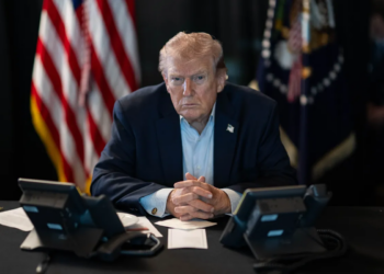 Donald Trump sentado frente a teléfonos con expresión seria