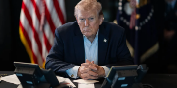 Donald Trump sentado frente a teléfonos con expresión seria