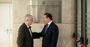 Dos hombres conversando frente a una placa conmemorativa de diplomáticos.