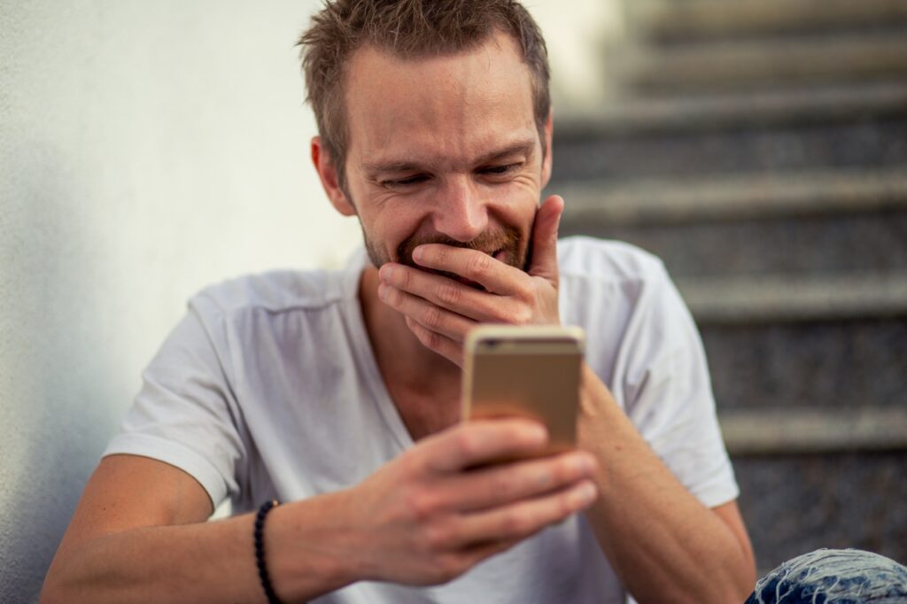 Hombre sonriente mirando su teléfono móvil mientras juega online