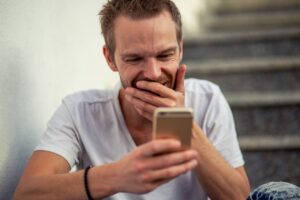 Hombre sonriente mirando su teléfono móvil mientras juega online