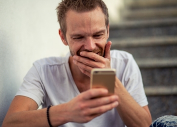 Hombre sonriente mirando su teléfono móvil mientras juega online