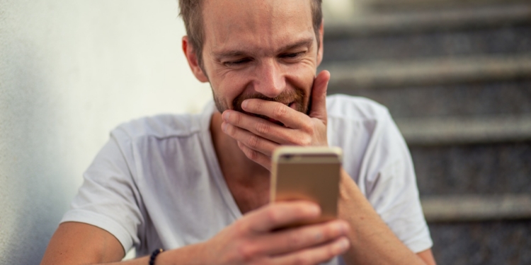 Hombre sonriente mirando su teléfono móvil mientras juega online