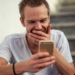 Hombre sonriente mirando su teléfono móvil mientras juega online