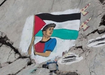 Mural de un joven sosteniendo una bandera palestina sobre escombros