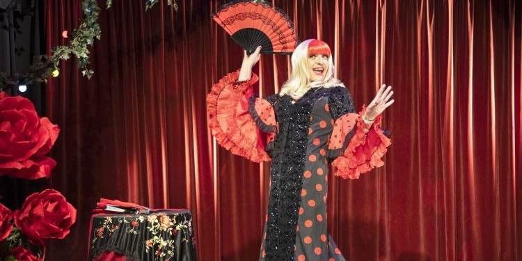 Artista drag con vestido de lunares y abanico en un escenario