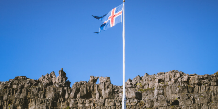 Bandera de Islandia ondeando contra un cielo azul claro.