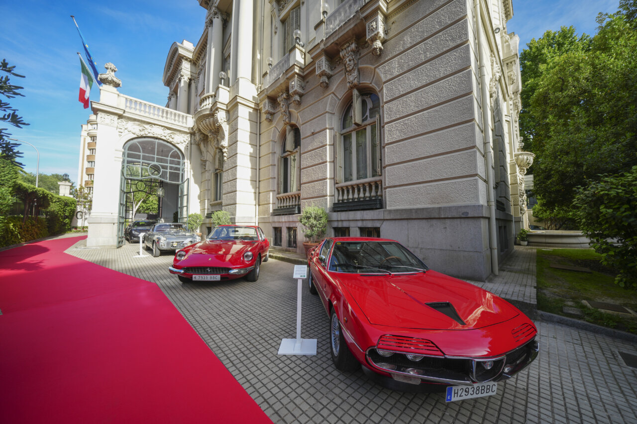 Tres coches clásicos rojos en la entrada de un edificio elegante en Madrid.