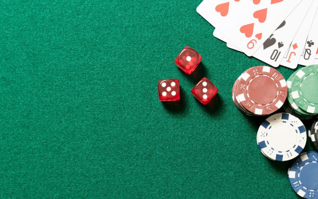 Mesa de juego con fichas de casino y dados rojos sobre fondo verde.