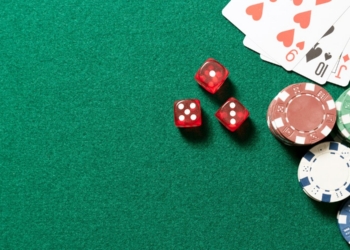 Mesa de juego con fichas de casino y dados rojos sobre fondo verde.