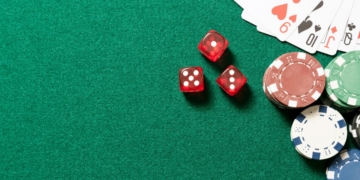 Mesa de juego con fichas de casino y dados rojos sobre fondo verde.