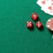 Mesa de juego con fichas de casino y dados rojos sobre fondo verde.