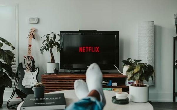 Persona relajándose en un sofá mientras ve Netflix en la televisión.