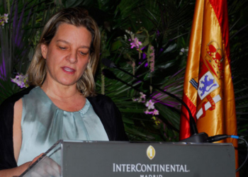 Ana Sálomon hablando en un evento oficial con la bandera de España de fondo