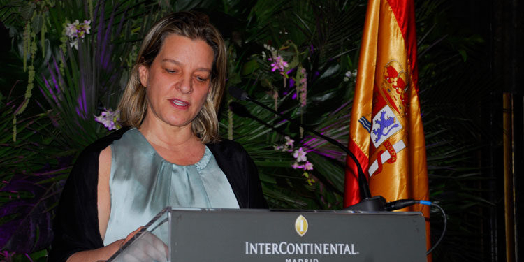 Ana Sálomon hablando en un evento oficial con la bandera de España de fondo