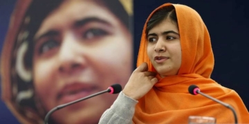 Malala Yousafzai hablando en una conferencia con un fondo difuminado.