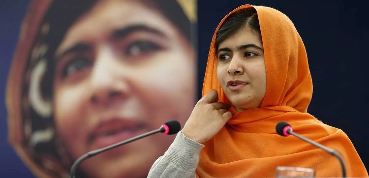 Malala Yousafzai hablando en una conferencia con un fondo difuminado.