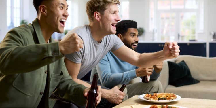Grupo de amigos emocionados viendo un partido deportivo en casa